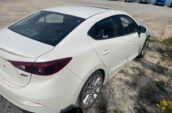 White car with Alloy wheels parked on gravel near a blue industrial building.