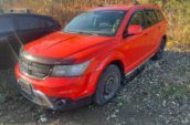 A bright red SUV parked on a rocky, grassy terrain next to a black vehicle.