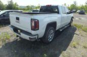 A white GMC pickup truck parked on a gravel area surrounded by greenery.
