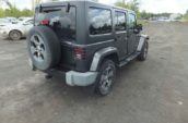 2018 Jeep Wrangler with a spare tire on the rear parked on a gravel lot, surrounded by trees and a cloudy sky.