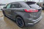 A gray SUV with rain-soaked windows and body is parked on a wet, gravel surface.