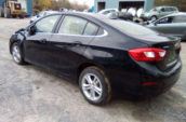 Black Chevrolet Cruze compact sedan with alloy wheels and chrome window trim, parked in a gravel lot surrounded by other vehicles