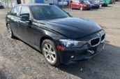 Black 2014 BMW 320i sedan parked on gravel lot outside auto repair shop with other vehicles in background