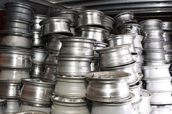 Stack of used and worn aluminum car rims piled together in a workshop or scrap yard